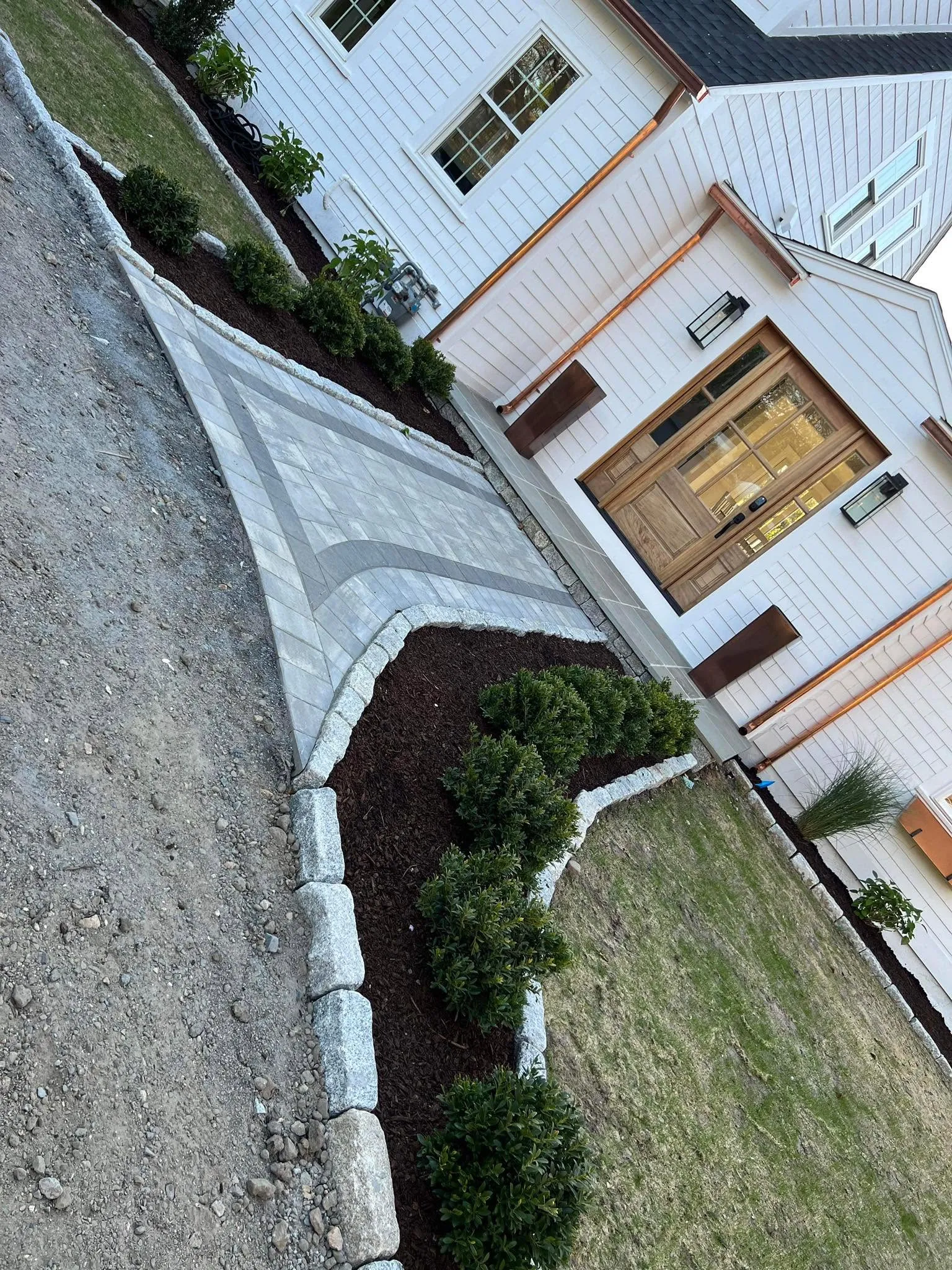 Curved paver walkway with mulched shrub beds beside a house